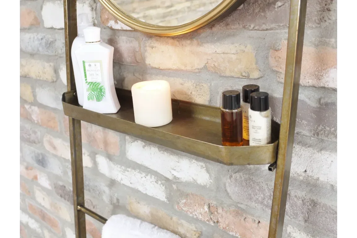 Gold metal bathroom shelf holding bottles and candle against exposed brick wall
