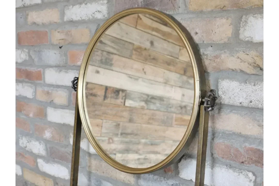 Round brass framed mirror with adjustable stand against exposed brick wall