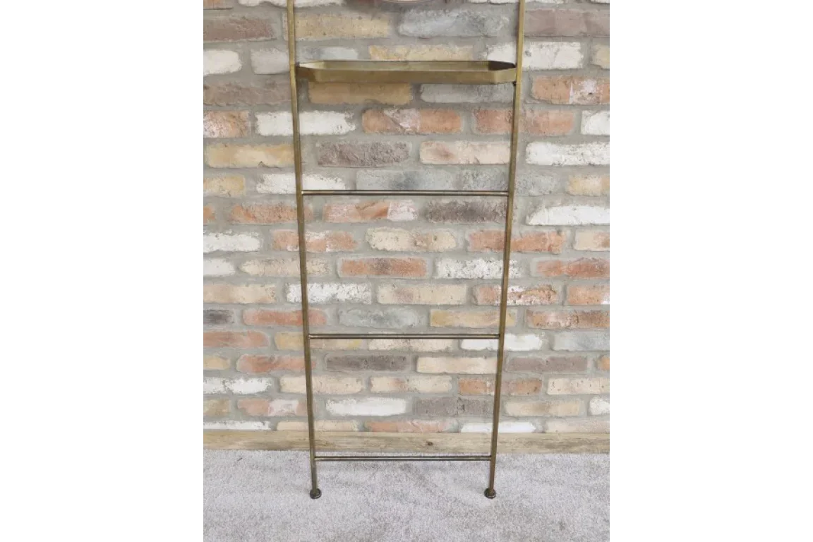 Brass metal ladder shelf with four rungs and tray against exposed brick wall