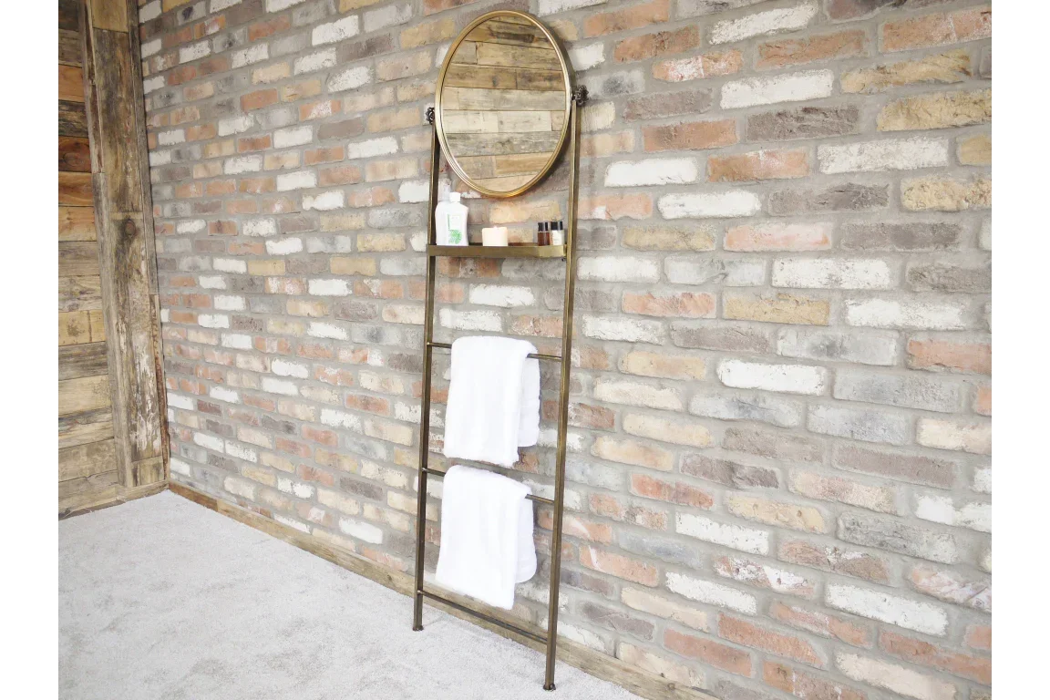 Metal ladder shelf with round mirror, toiletries, and towels against exposed brick wall
