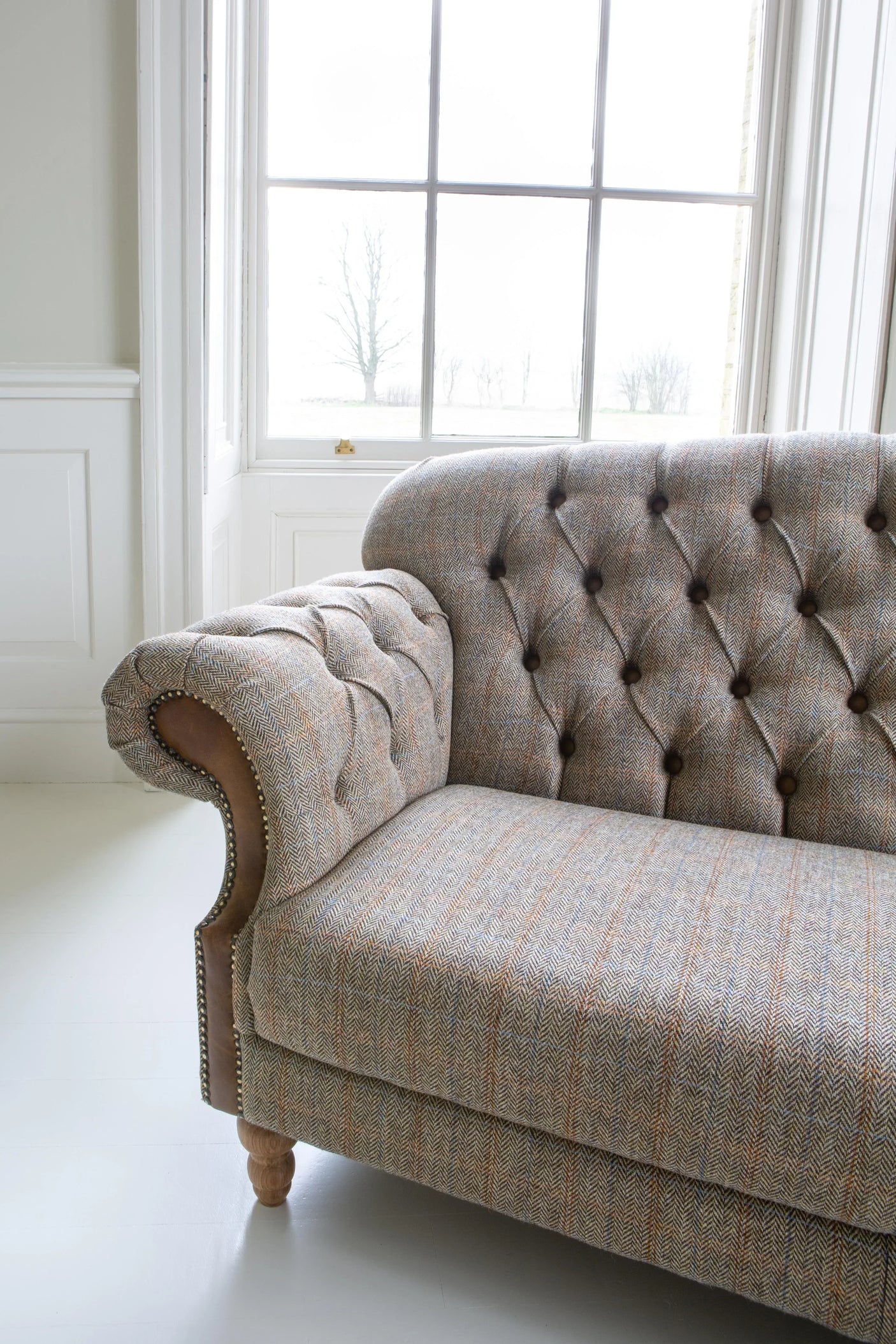 Close-up of grey fabric Chesterfield sofa with button tufting and wooden leg in bright room