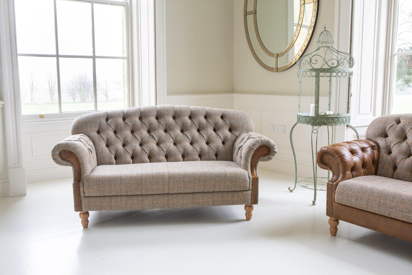 Grey button-tufted fabric sofa with rolled arms and wooden legs in a bright living room
