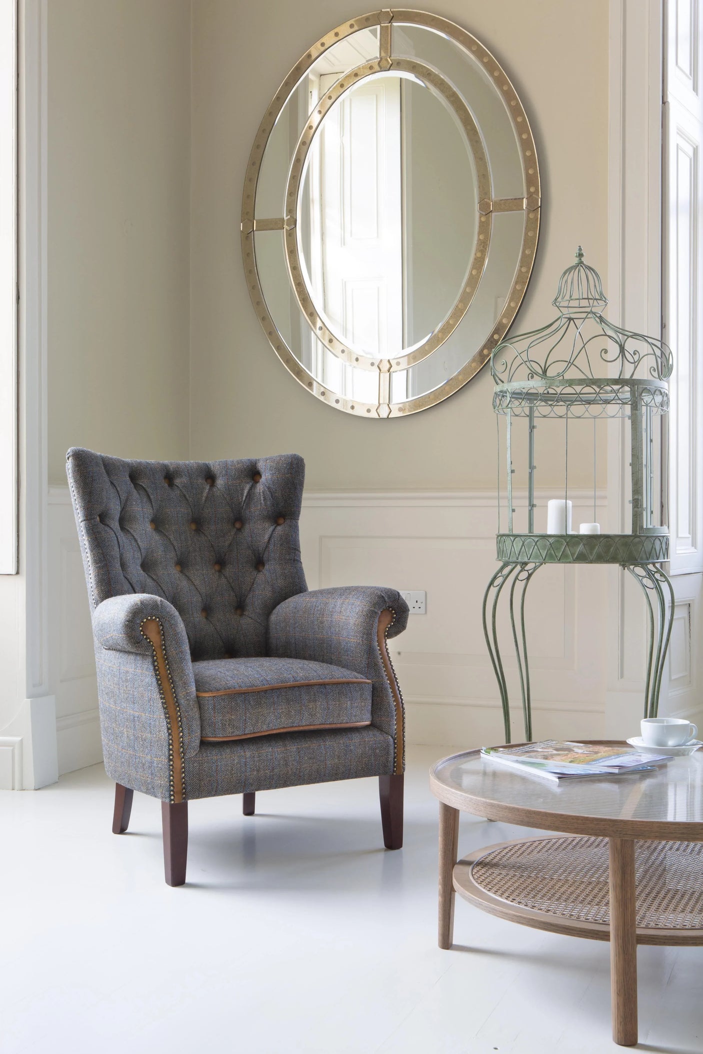 Grey buttoned armchair with stud detailing beside round wooden coffee table in bright living room