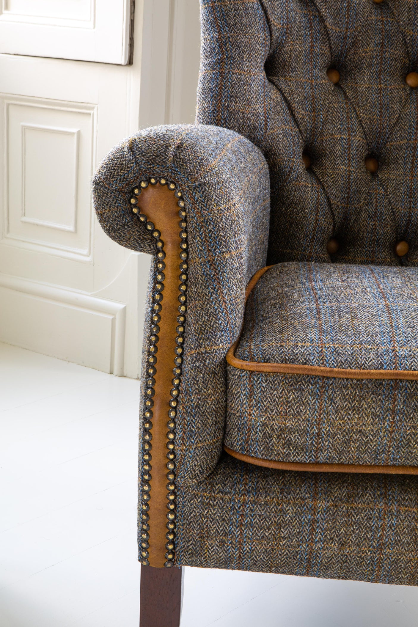 Tweed armchair with button tufting, studded trim, and wooden leg in a white room