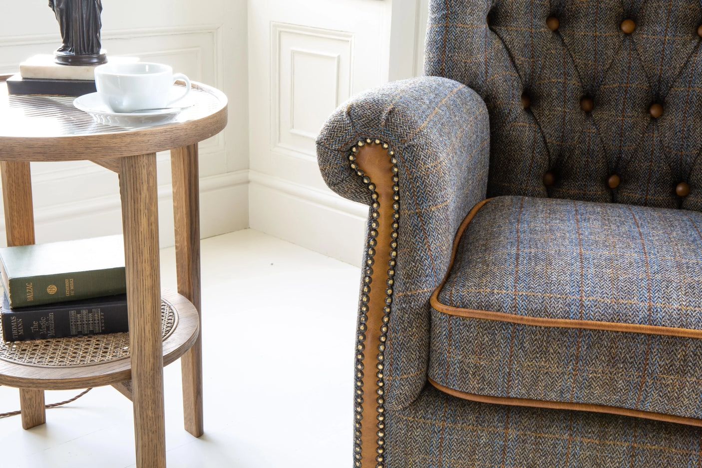Tweed armchair with buttoned back and studded detail beside wooden side table with cup