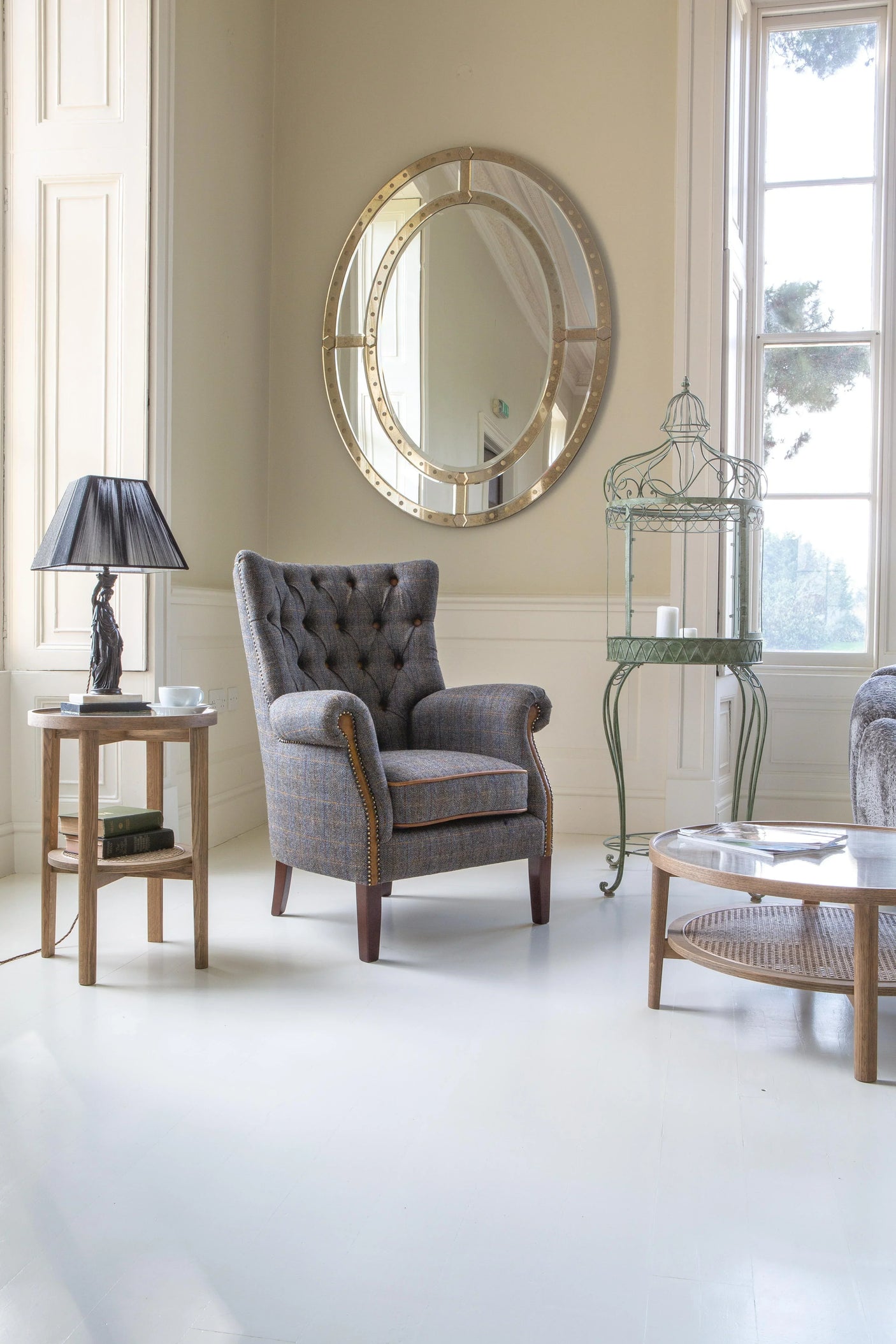 Grey plaid armchair with button tufting beside wooden table and round wall mirror