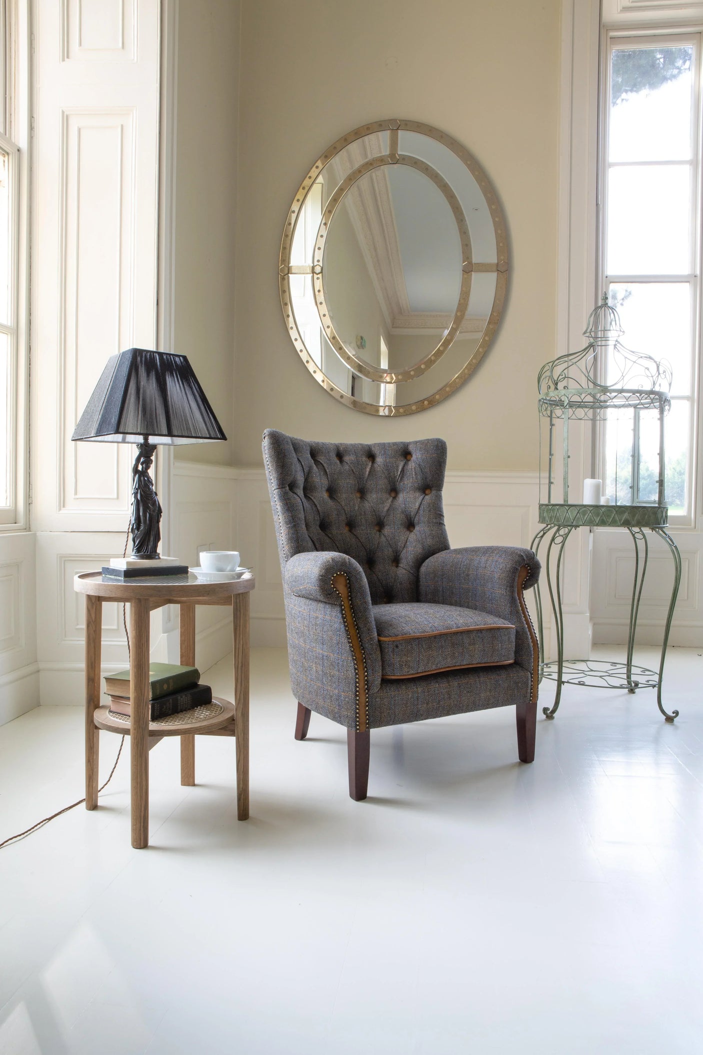 Tufted armchair with grey upholstery beside wooden side table and decorative round mirror