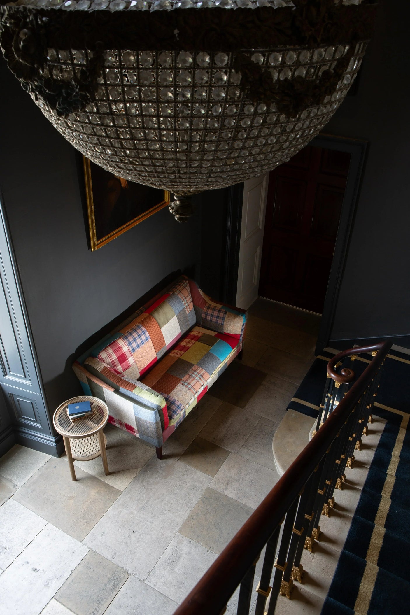 Patchwork fabric sofa with wooden legs in hallway, next to round cane side table and stairs