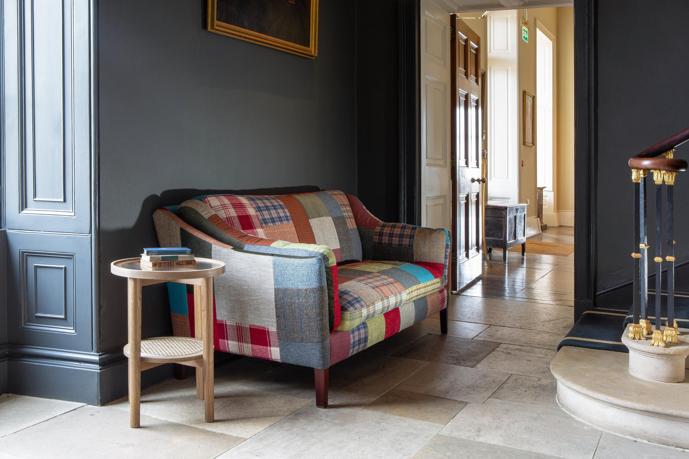 Patchwork fabric sofa with wooden legs beside round oak side table in hallway