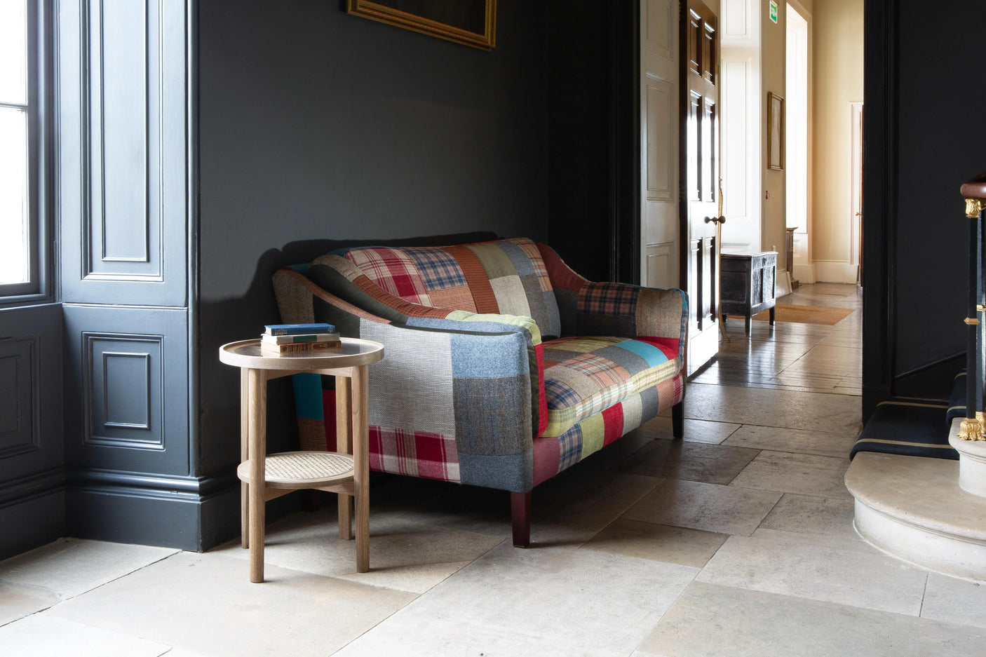 Patchwork fabric sofa with wooden legs in hallway, round side table with books beside