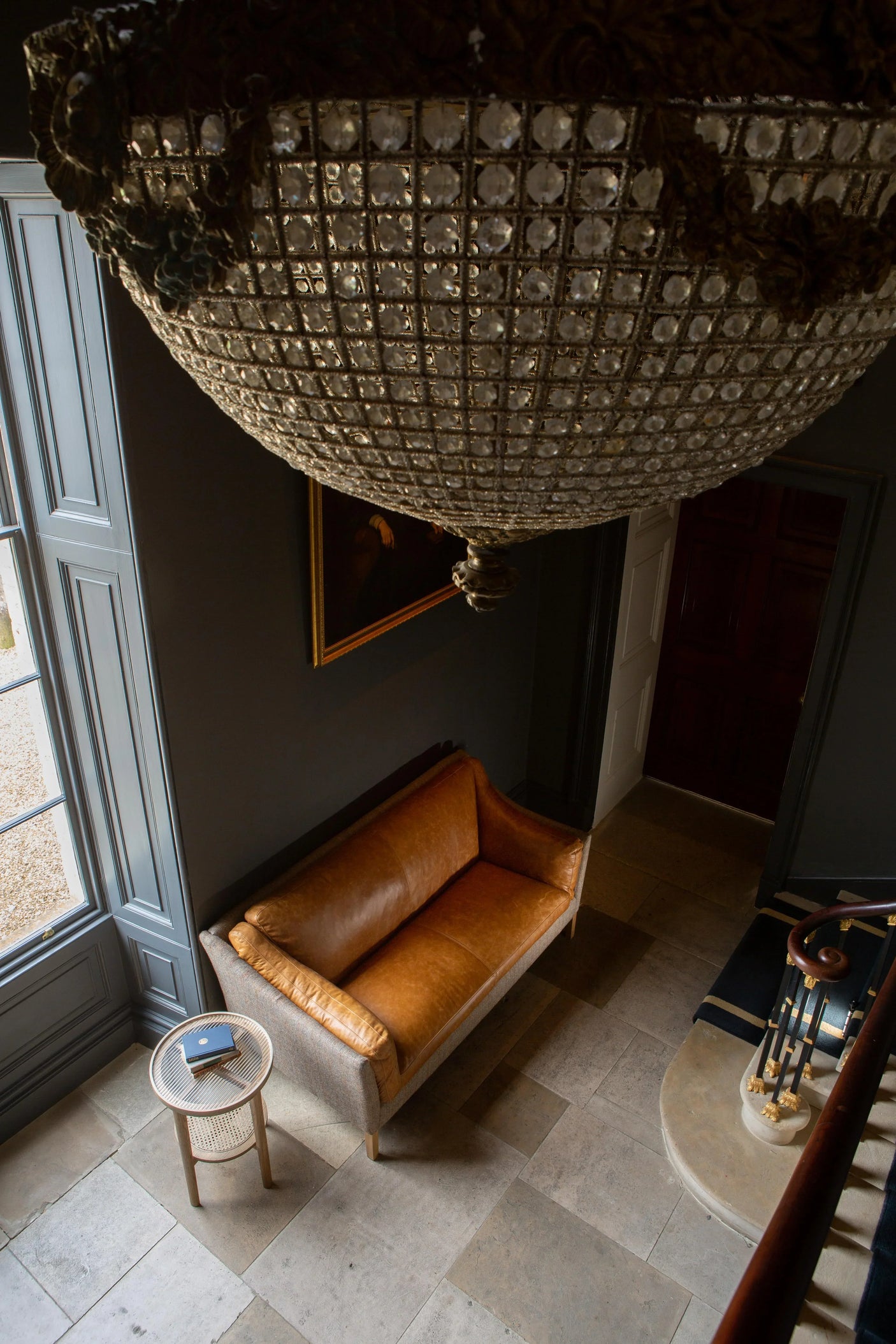 Tan leather sofa with light wood frame in entryway beside round side table and chandelier