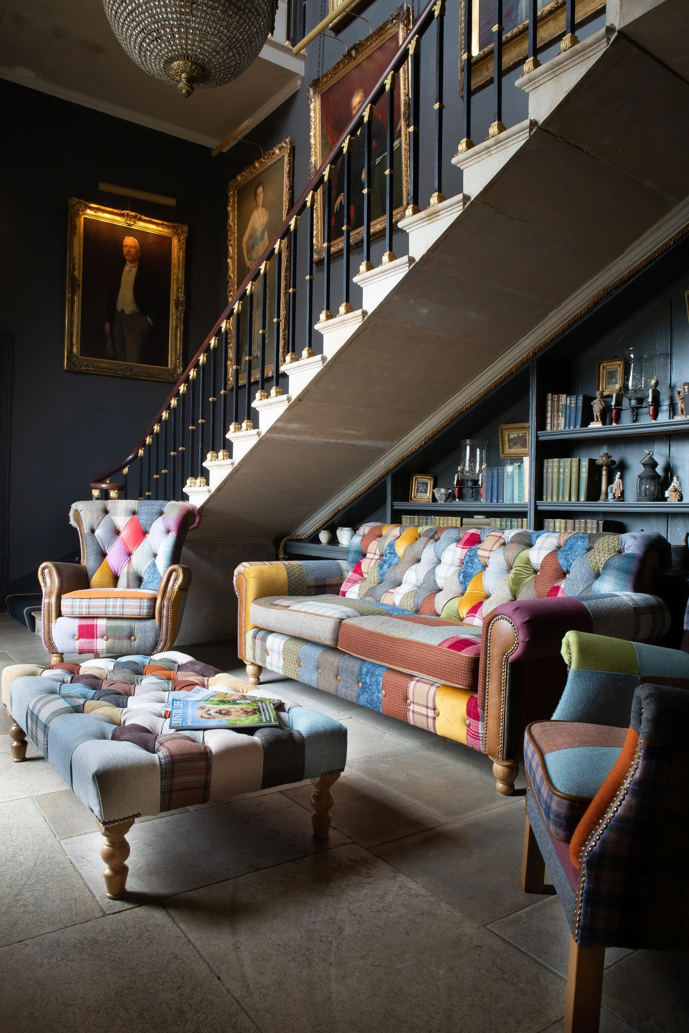 Patchwork armchair, sofa, and footstool set in traditional lounge with staircase and portraits