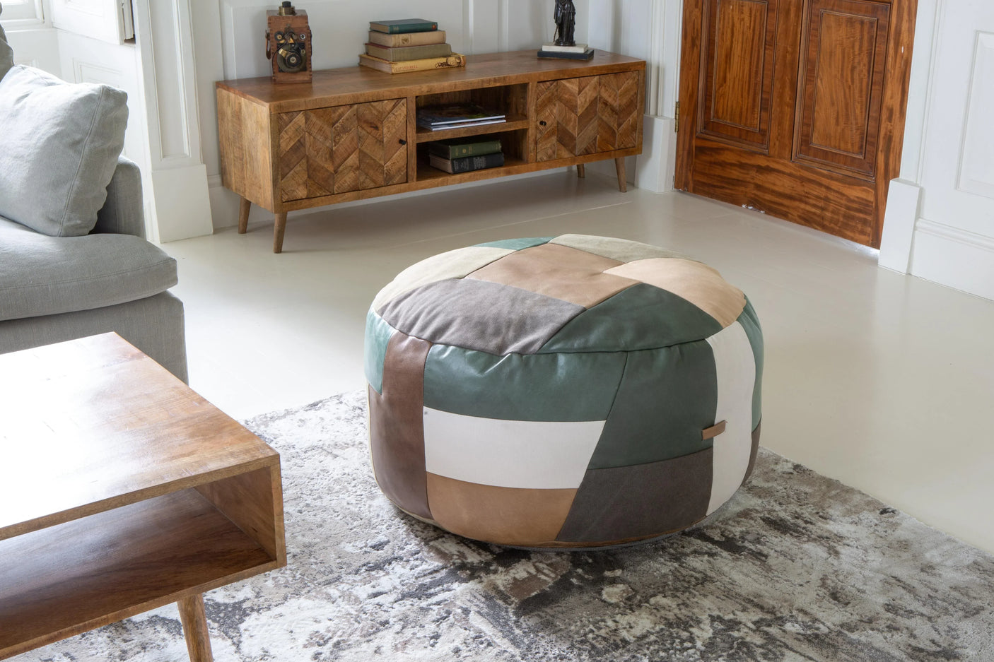 Patchwork leather pouffe on patterned rug in bright living room with wooden furniture
