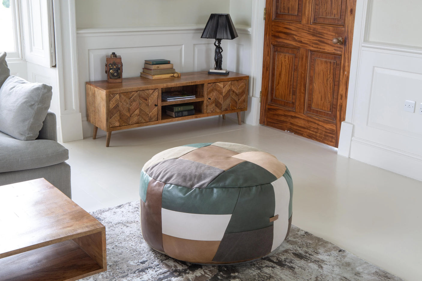Patchwork leather pouffe on grey rug in modern living room with wooden sideboard