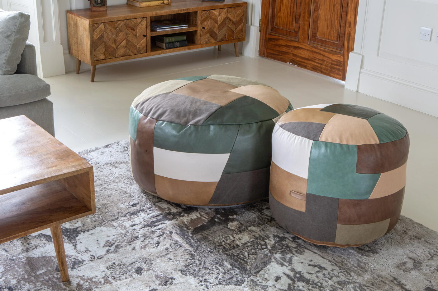 Patchwork leather pouffes in living room on patterned rug with wooden furniture