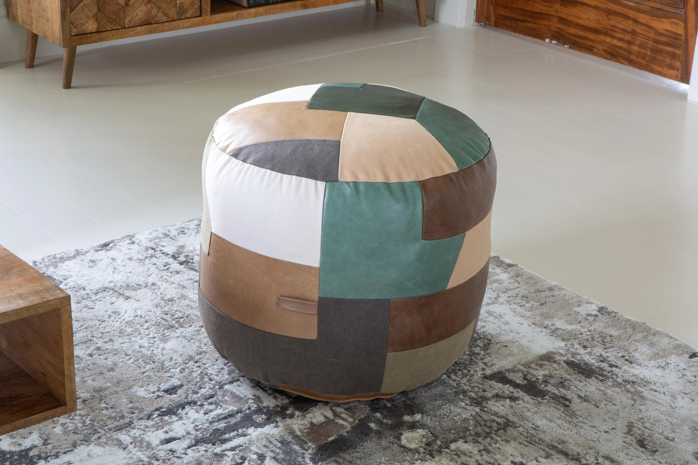 Patchwork fabric pouffe with earth tones and green accent on patterned rug in living room