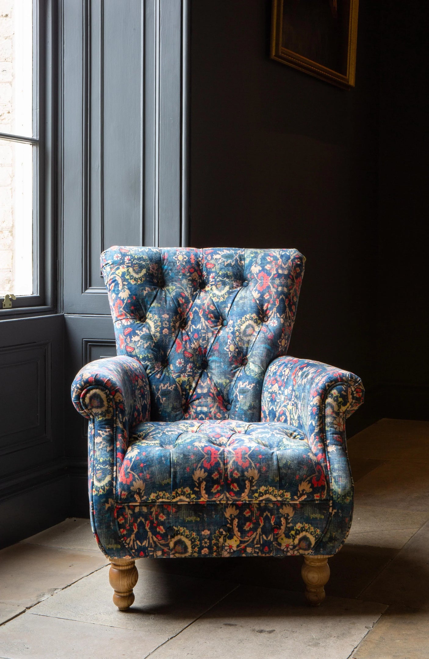Patterned fabric armchair with button-tufted back and wooden legs by window