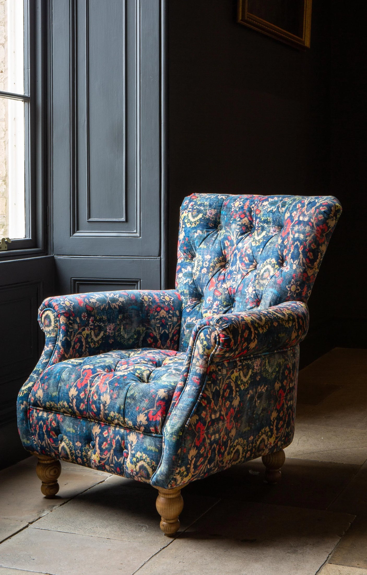 Blue floral fabric armchair with button back and wooden legs by window