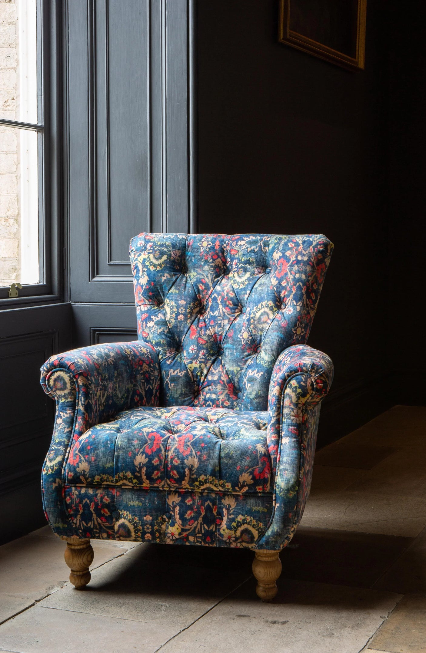 Patterned fabric armchair with wooden legs in front of dark wall and window
