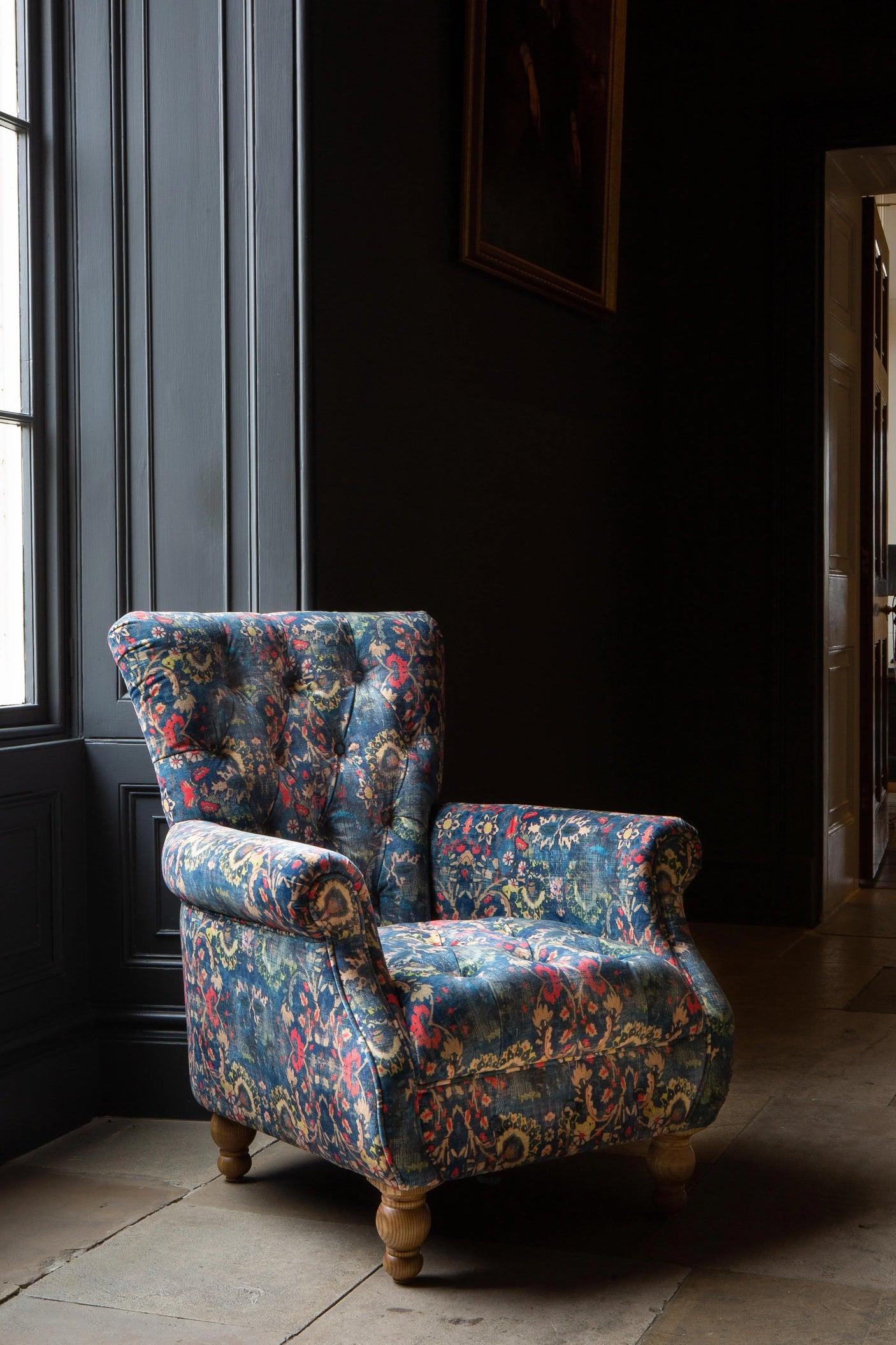 Floral upholstered armchair with buttoned backrest and wooden legs in a dark room
