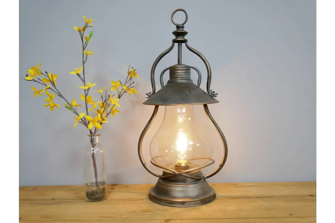 Vintage lantern table lamp with glass bulb beside yellow flowers in a clear vase on wood