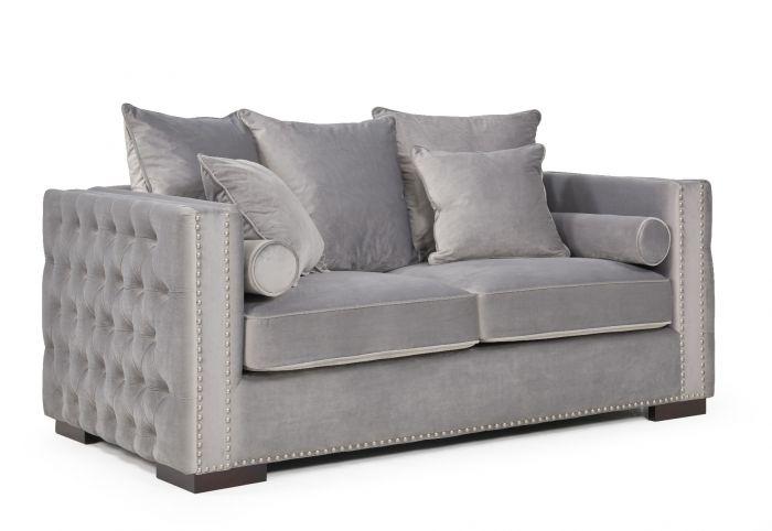 Grey velvet two-seater sofa with buttoned arms, nailhead trim and scatter cushions, angled view