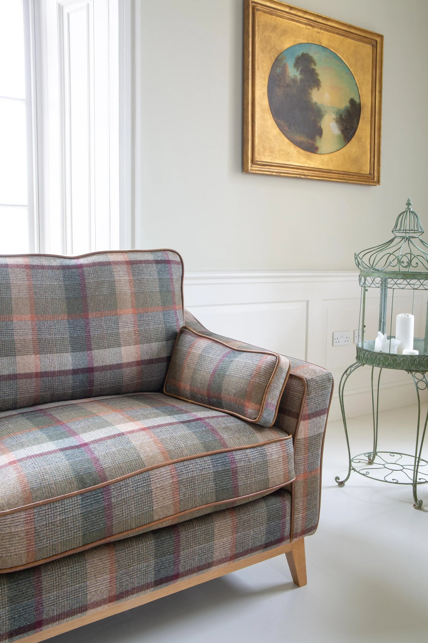 Plaid fabric sofa with wooden legs in bright living room, side table and wall art