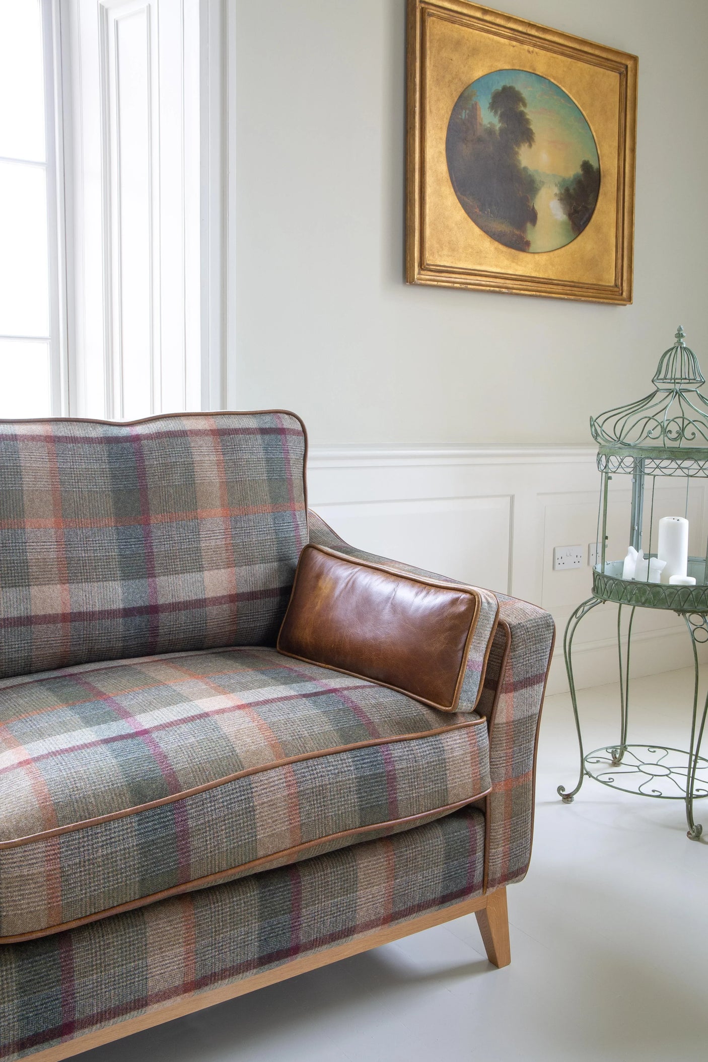 Plaid upholstered sofa with leather cushion in bright lounge, next to metal side table