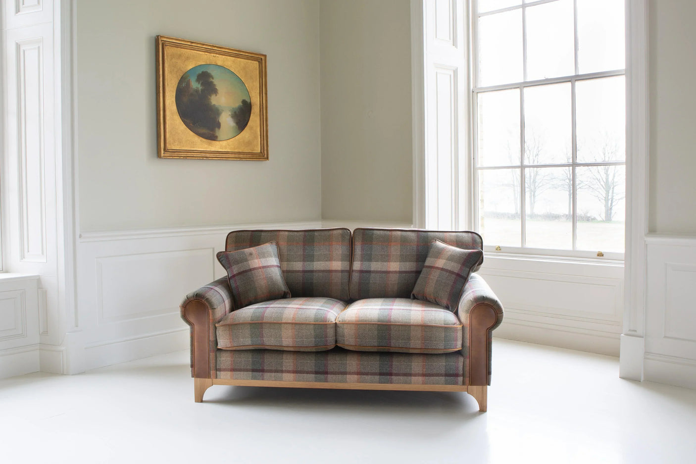 Plaid fabric two-seater sofa with wooden legs in bright living room, includes matching cushions