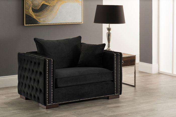 Black velvet armchair with studded arms and cushions, next to glass side table and lamp