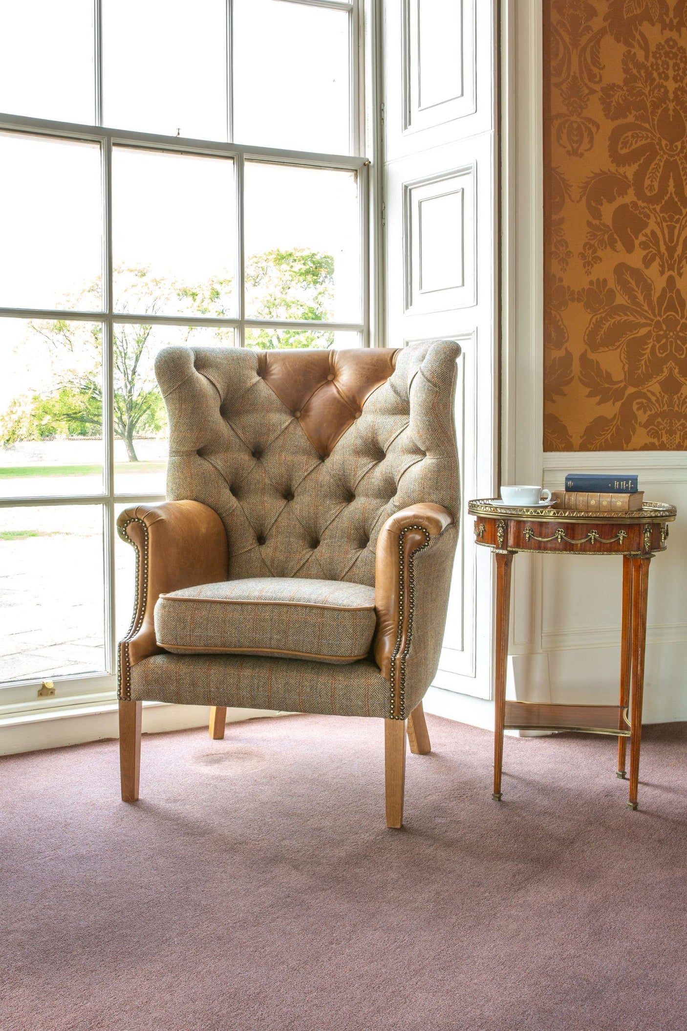 Button-tufted armchair with tweed fabric and tan leather accents beside window and side table
