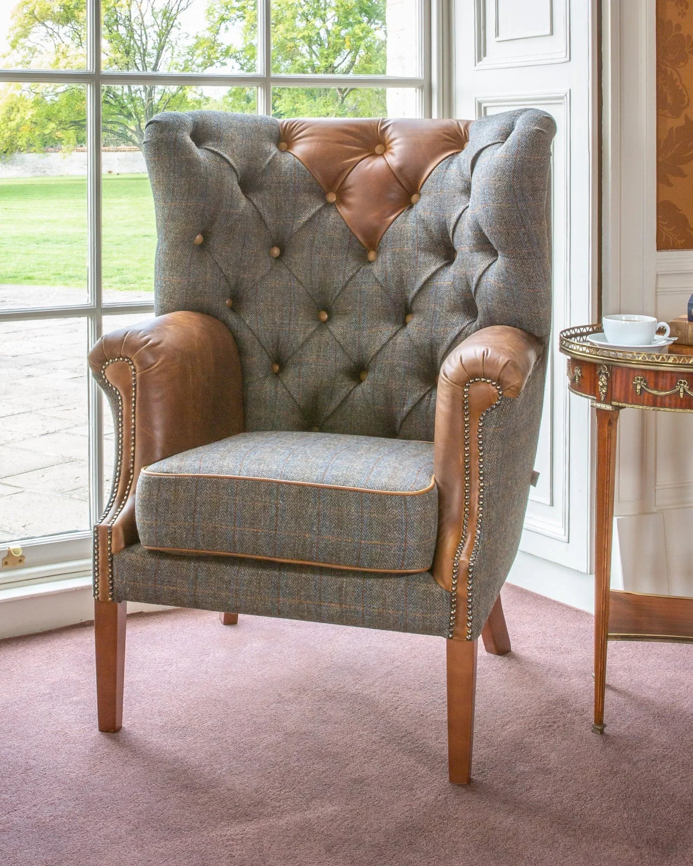 Button-tufted wingback armchair with brown leather and grey fabric upholstery by window