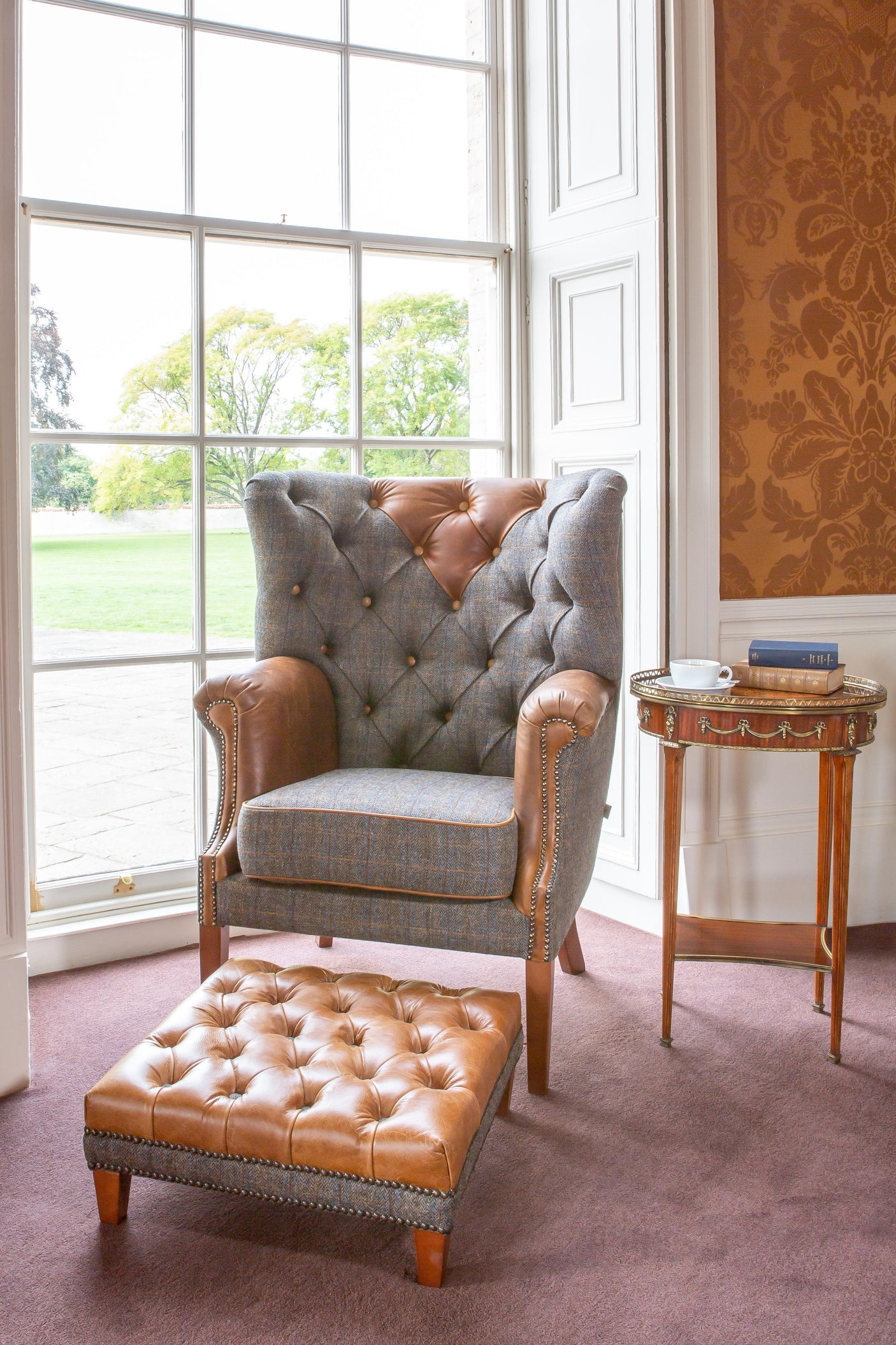 Leather and fabric armchair with matching footstool beside window and wooden side table