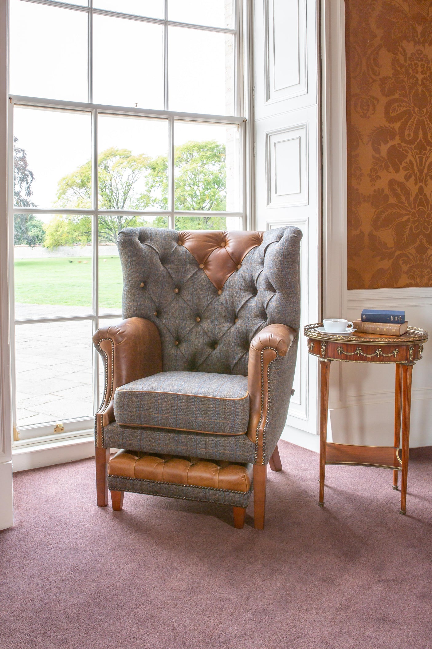 Tufted armchair with plaid fabric and brown leather accents beside window and side table