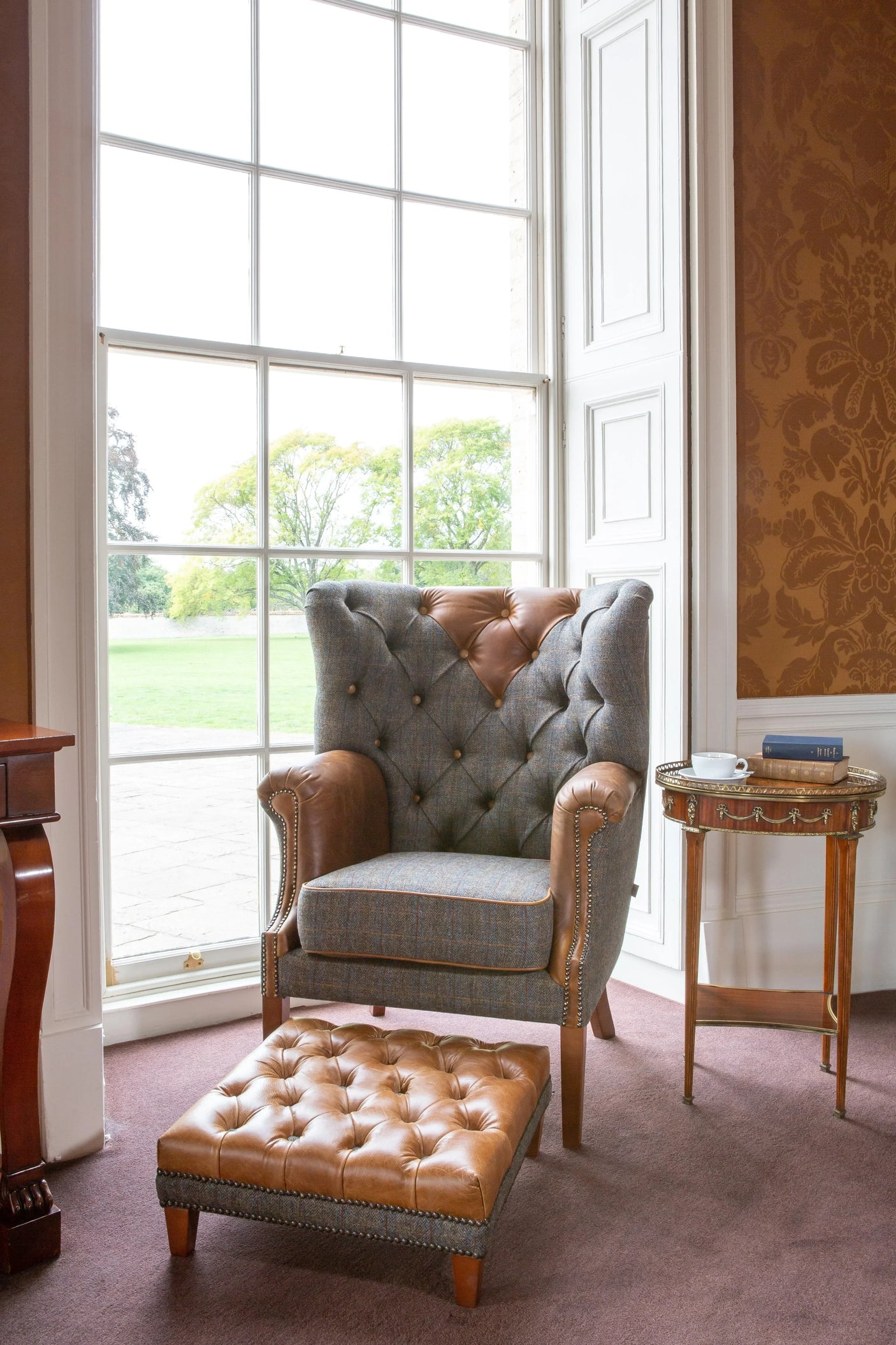 Leather and tweed armchair with matching footstool by large window in classic living room