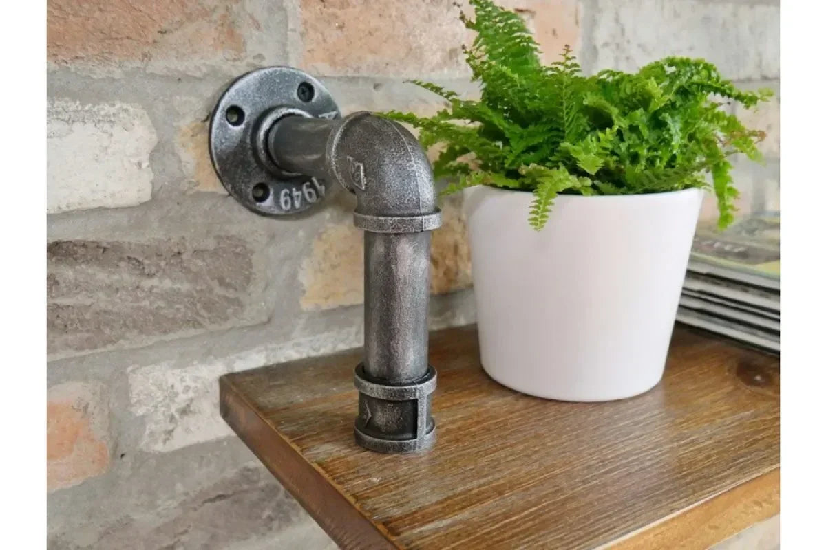 Industrial pipe shelf bracket on wood shelf with white plant pot and green fern