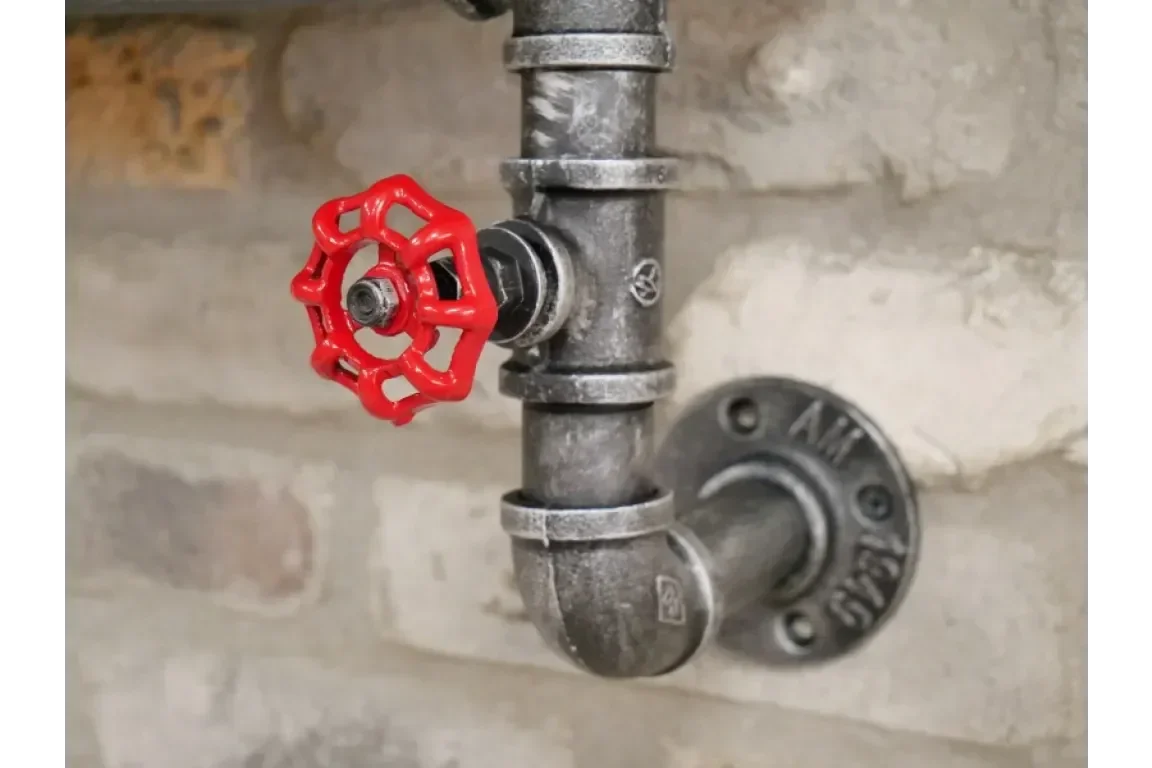 industrial pipe wall fitting with red valve handle against exposed brick background