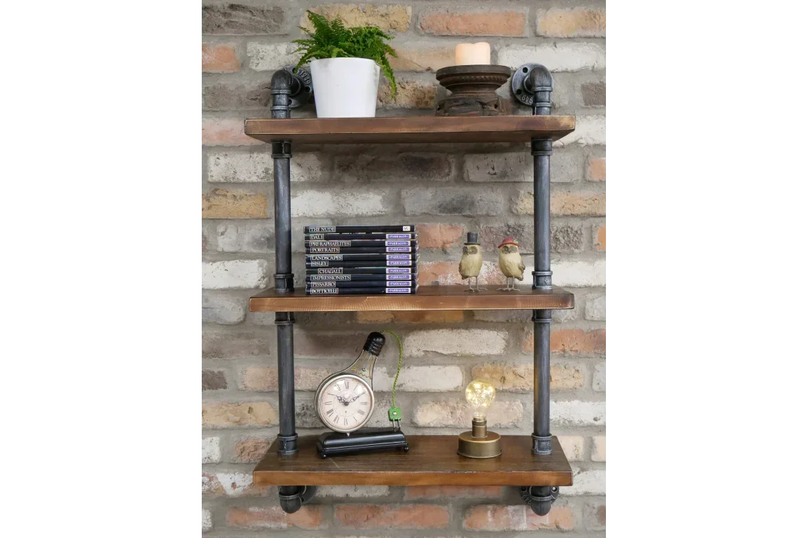 Industrial pipe wall shelf with wooden shelves, books, clock, lamp, and decor against brick wall