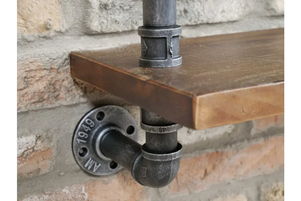 Industrial pipe bracket supporting wooden shelf on exposed brick wall