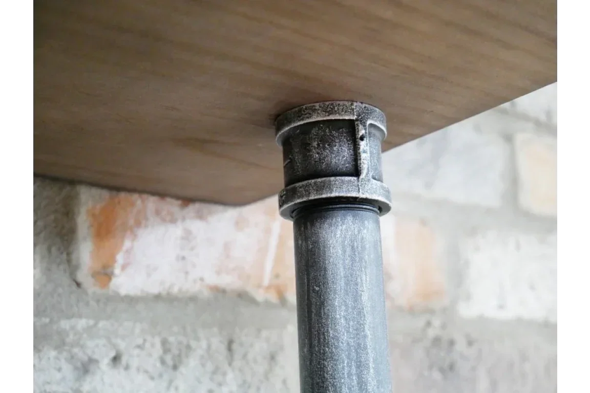 Industrial metal table leg attached to wooden tabletop with exposed brick wall background
