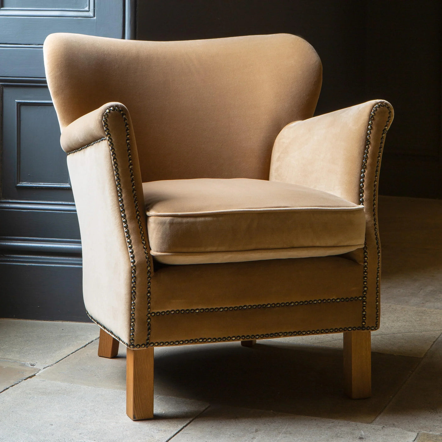 Tan velvet accent armchair with studded trim and wooden legs in modern interior