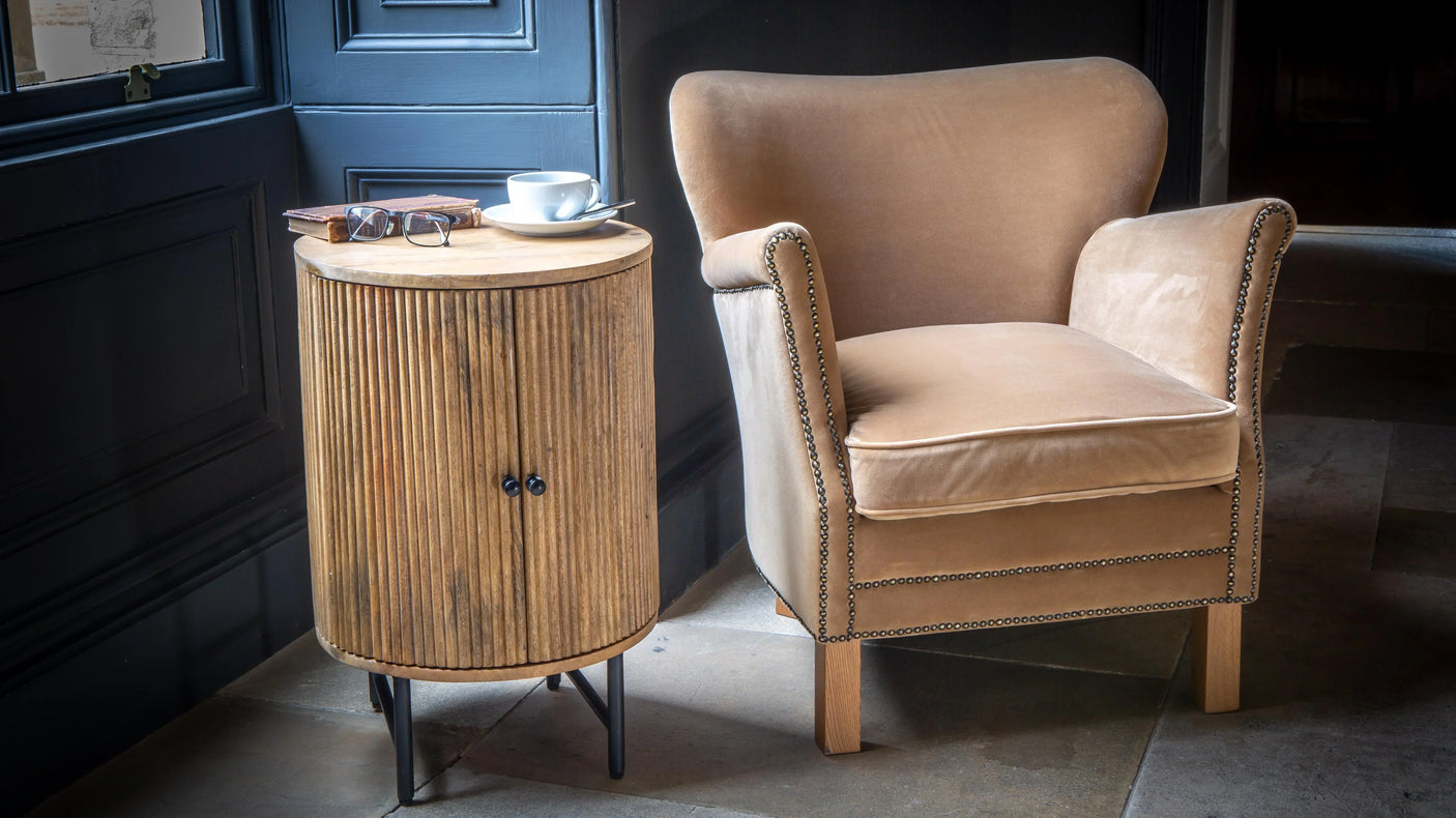 Velvet armchair with nailhead trim and round wood side table in cosy corner setting