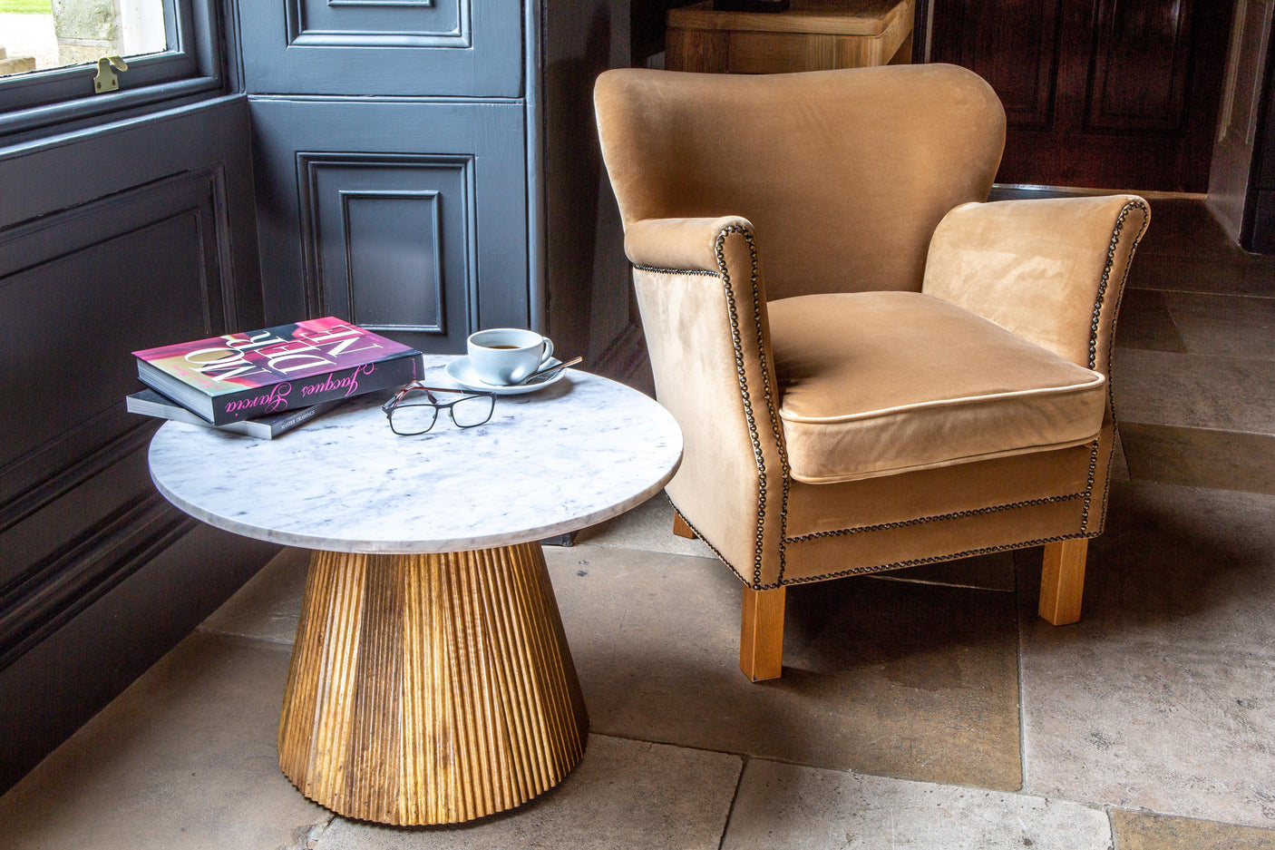 Velvet armchair with stud detail beside round marble coffee table with books and cup