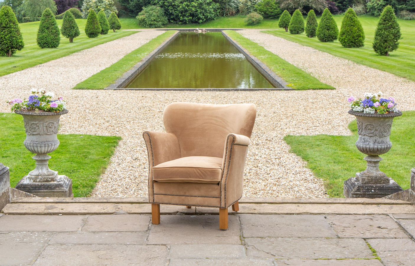 Beige fabric armchair with wooden legs set in a formal garden with gravel path and pond