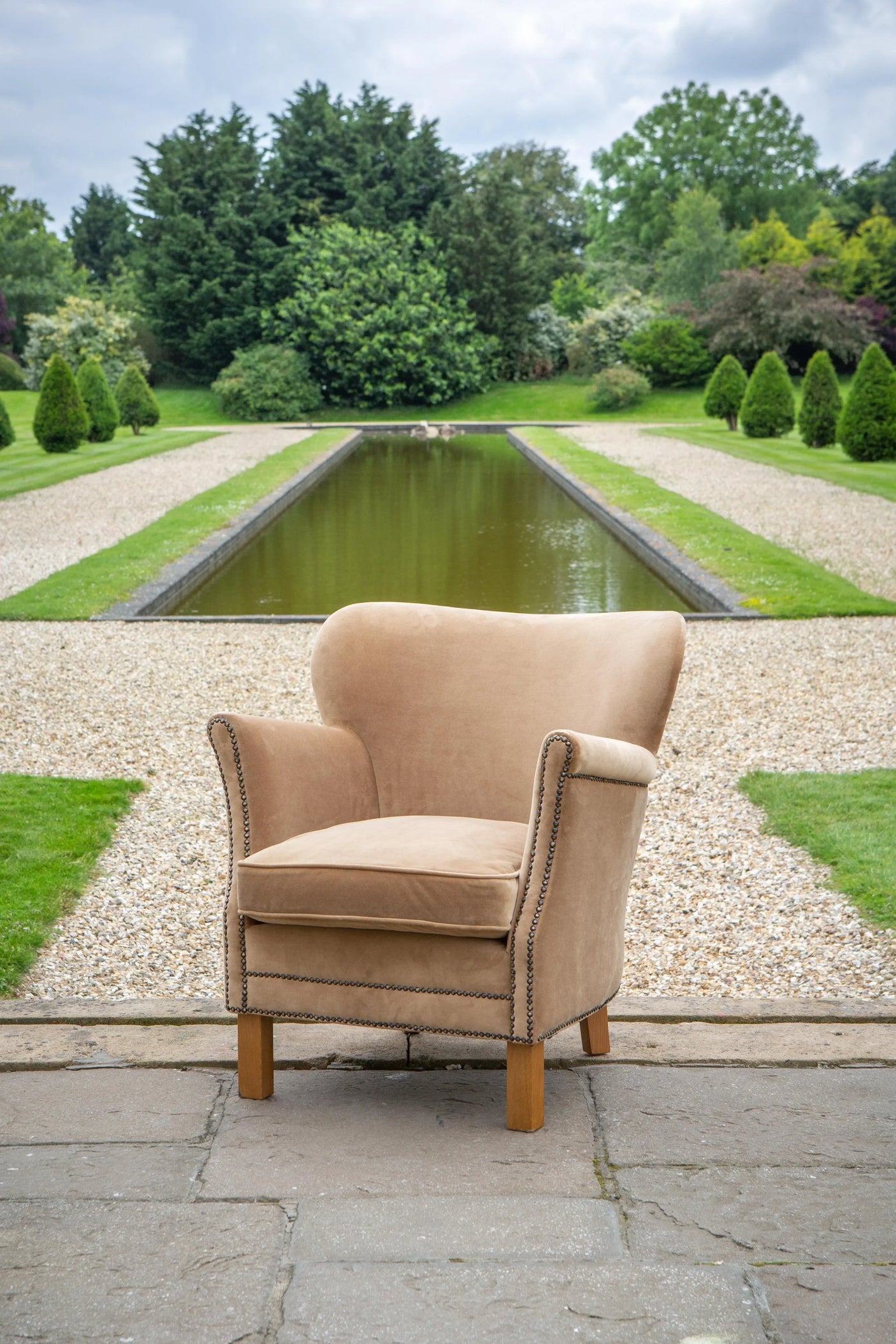 Beige fabric armchair with wooden legs and stud detailing, placed outdoors on stone patio