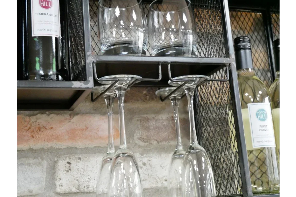 Wall mounted metal wine rack with hanging wine glasses and bottles on brick background
