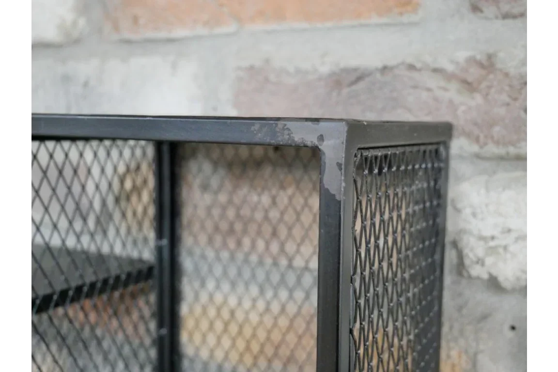 Black metal mesh furniture corner with industrial frame detail against brick wall