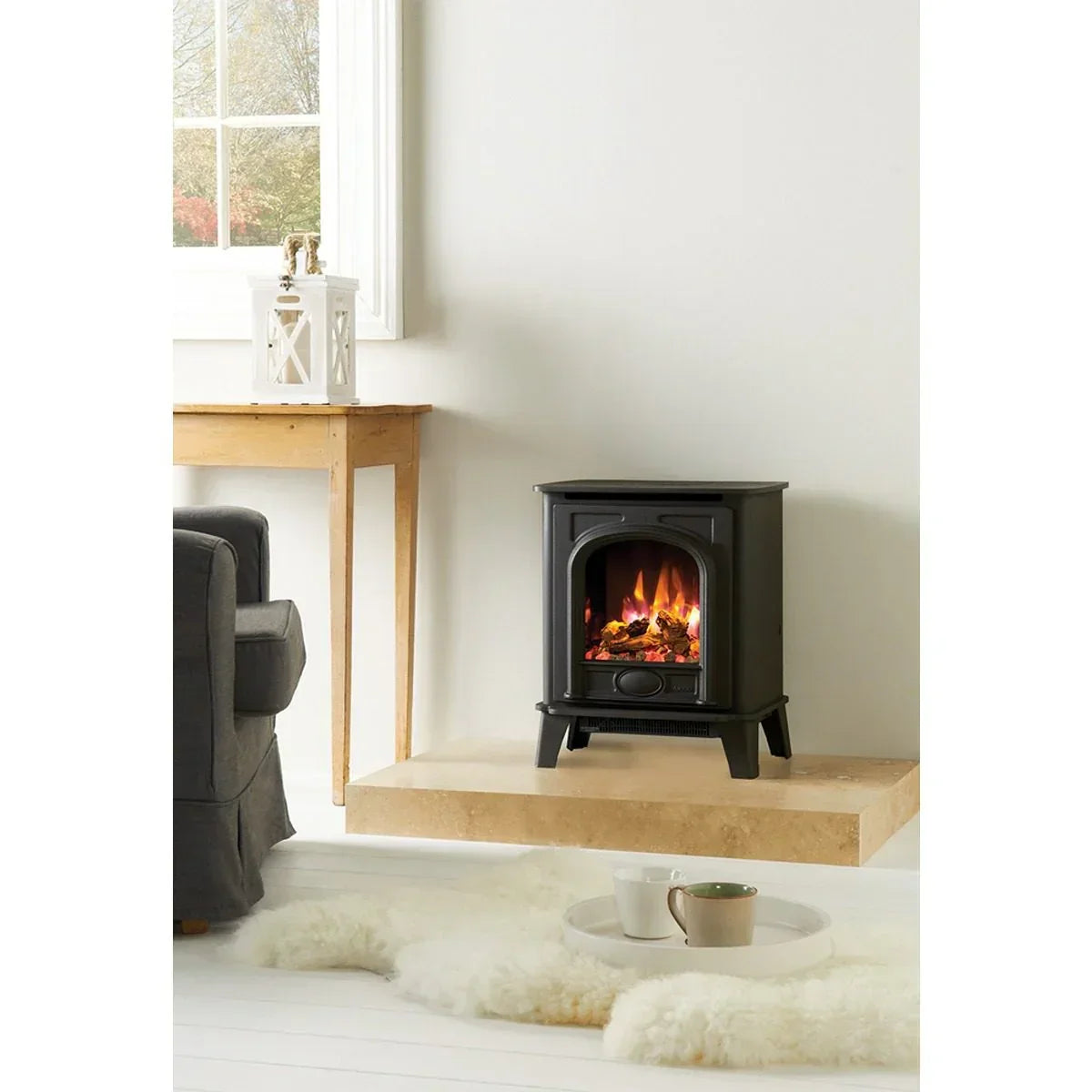 Black electric stove heater on stone hearth in modern living room with white decor
