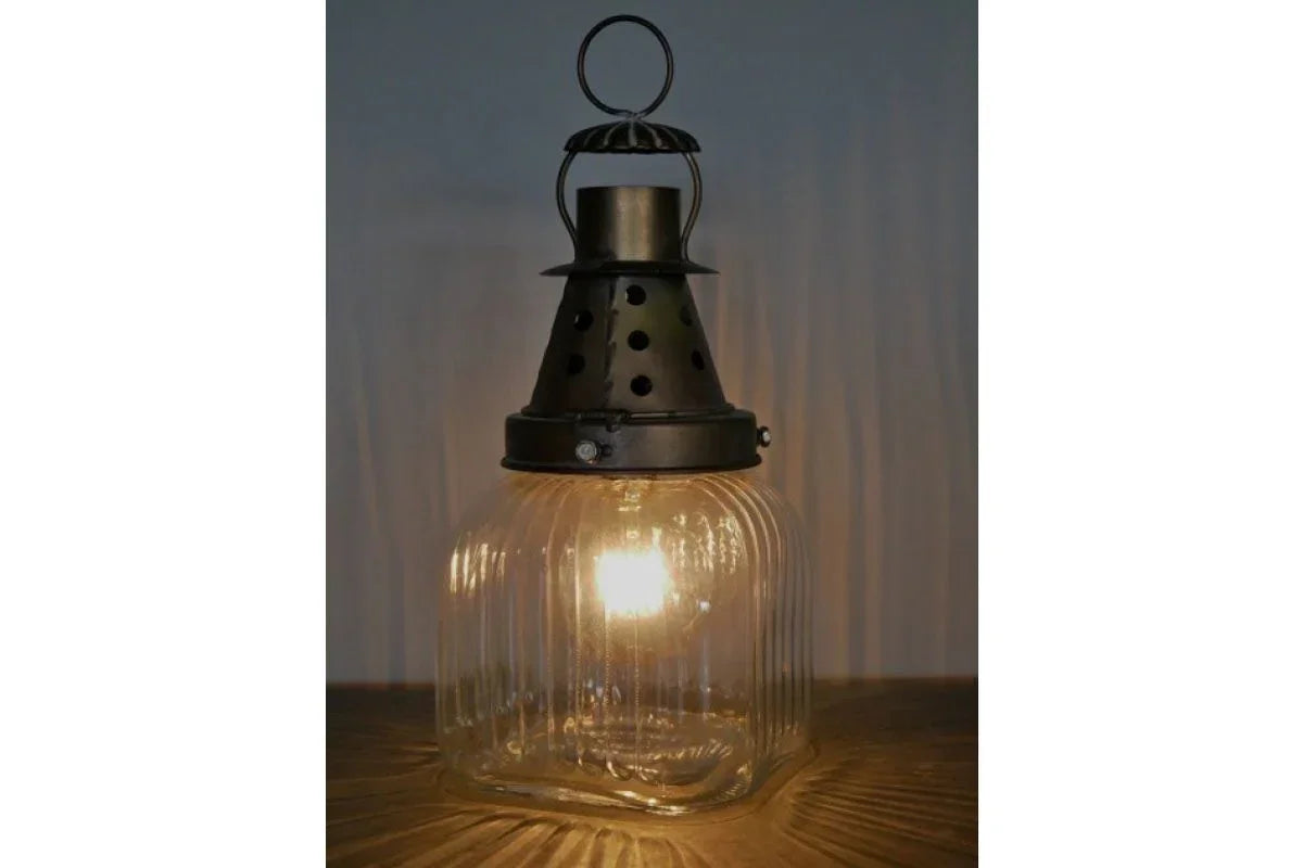Vintage glass lantern lamp with ribbed base and metal top illuminated on table