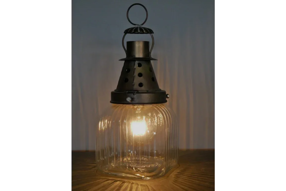 Glass and metal lantern lamp with warm light on wooden surface